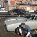 Image from Grand Theft Auto 5 showing Franklin crouched behind a car while being shot at.